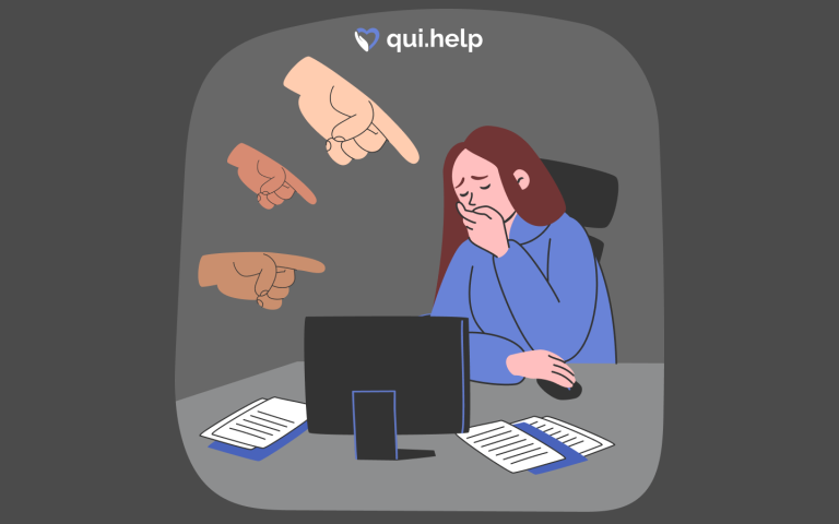 Ілюстрація до статті про булінг на роботі: жінка сидить за комп’ютером, прикривши обличчя рукою, виглядає пригніченою, у її бік спрямовані кілька вказівних пальців, що символізує мобінг, критику та тиск у колективі. Логотип qui.help зверху.